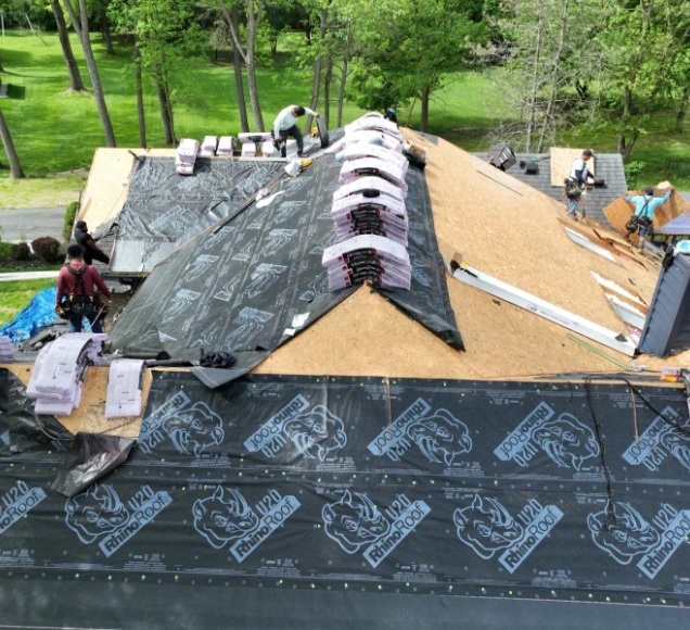 Crew laying new shingles over underlayment on a partly stripped roof