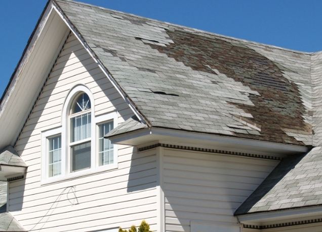 Weathered shingle roof with bare and discolored patches above a white sided gable