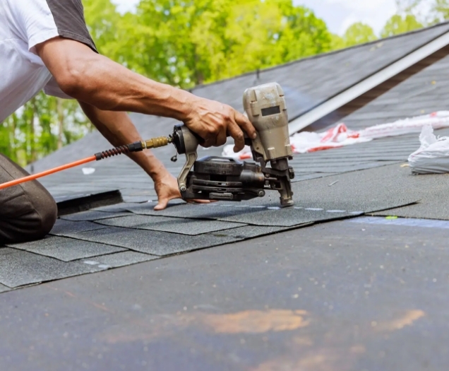 Roofer fastening new dark asphalt shingles with a pneumatic nail gun