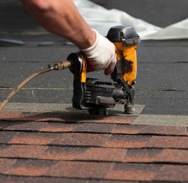 Nail gun fastening a new course of shingles above older red brown shingles