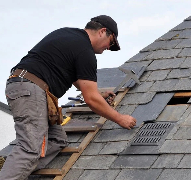 Roofer replacing shingles around a roof vent on a gray shingle roof