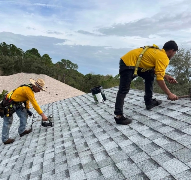 Two roofers in harnesses working on a light gray shingle roof